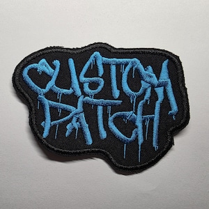 Puede incluir: Un parche bordado negro con las palabras "CUSTOM PATCH" en letras azules goteantes. El parche tiene una forma irregular y está diseñado para ser cosido o planchado en ropa o accesorios.
