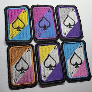May include: Six Ace of Spades patches with a colourful, geometric design. Each patch features a spade symbol and the letter "A". The patches have a black border and are in various colour combinations, including pink, yellow, blue, and orange.