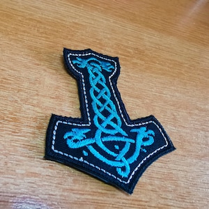 Puede incluir: Un parche bordado azul y negro de un martillo Mjolnir nórdico con un diseño de nudo celta.