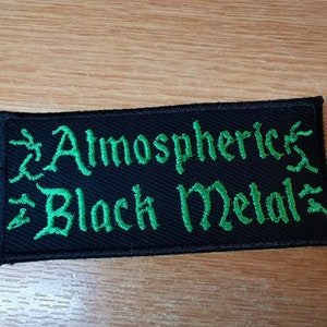 Op de afbeelding: Zwarte patch met groene geborduurde tekst die "Atmospheric Black Metal" luidt.