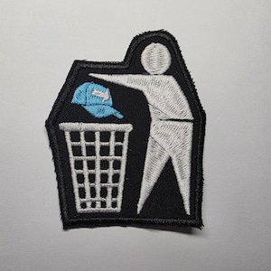 Könnte beinhalten: Gestickter Aufnäher mit einer Strichmännchen-Figur, die eine blaue Baseballkappe in einen Mülleimer wirft. Der Aufnäher ist schwarz mit weißen und blauen Akzenten. Das Design ist eine humorvolle Darstellung.