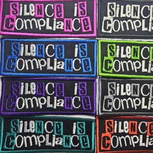 May include: A collection of embroidered patches, each displaying the text "SILENCE IS COMPLIANCE". The patches have black backgrounds with the text in white, pink, blue, green, purple, and orange.
