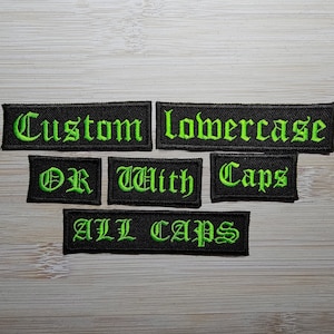 Könnte beinhalten: Vier schwarze Stoffpatches mit grünem Sticktext. Die Patches lauten "Custom lowercase", "OR with", "Caps" und "ALL CAPS".