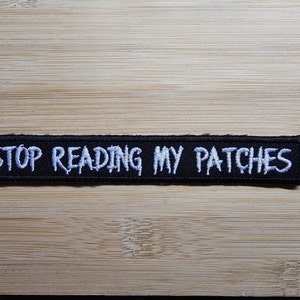 Könnte beinhalten: Schwarzer gestickter Aufnäher mit weißem Text, der "STOP READING MY PATCHES" lautet.