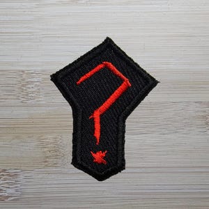 May include: A black and red embroidered patch shaped like a diamond with a question mark inside.
