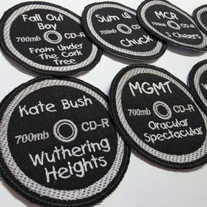 May include: Black and white embroidered patches in the shape of CDs. Each patch features a band name, album title, and "700mb CD-R" text. Bands include Fall Out Boy, Sum 41, MCR, Kate Bush, and MGMT.