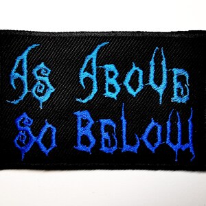 May include: Black rectangular embroidered patch with the words "As Above, So Below" in stylized blue lettering. The patch has a textured appearance and is likely designed to be sewn onto clothing or accessories.