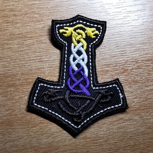 May include: Black embroidered patch of a Norse hammer with a purple, white, and yellow braided knot design.
