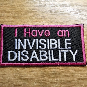 Può includere: Toppa ricamata nera con cuciture rosa. La toppa riporta la scritta "I Have an Invisible Disability".