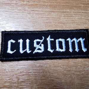 以下が含まれることがあります： 黒色の布地に、ゴシック体で「custom」と白く刺繍された文字が書かれたパッチ