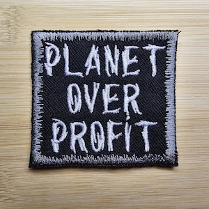 Puede incluir: Parche bordado negro con texto blanco que dice "Planet Over Profit".