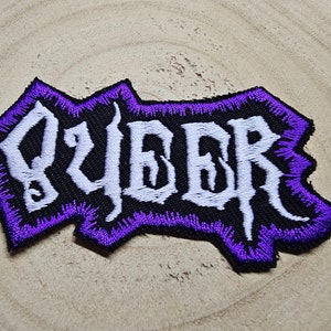 Peut inclure: Patch brodé de couleur violet et blanc avec le mot "JUDAS" dans une police gothique.