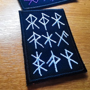 May include: Black fabric patch with white embroidered runes. The runes are arranged in three rows of three.