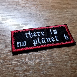以下が含まれることがあります： 赤いステッチが付いた黒い刺繍パッチ。パッチには「there is no planet b」と書いてあります。