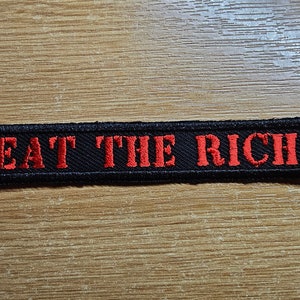 May include: Black embroidered patch with red lettering that reads "EAT THE RICH".