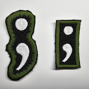 May include: Two green embroidered patches with white semicolon symbols. The larger patch is shaped like a semicolon. The smaller patch is rectangular.