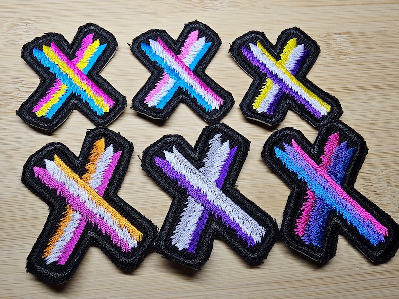 May include: Six embroidered iron-on patches in the shape of an 'X' with different color combinations of white, pink, blue, purple, yellow, and orange.