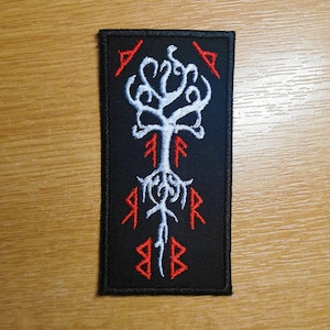 Peut inclure: Patch brodé noir avec un motif d'arbre blanc et des runes rouges. L'arbre a un tronc épais et des branches qui s'étendent. Les runes sont disposées autour de l'arbre.