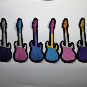 May include: Six embroidered guitar patches in various colours: purple, pink, blue, yellow, and orange. Each patch has a black border and a white neck. The patches are arranged in a row.