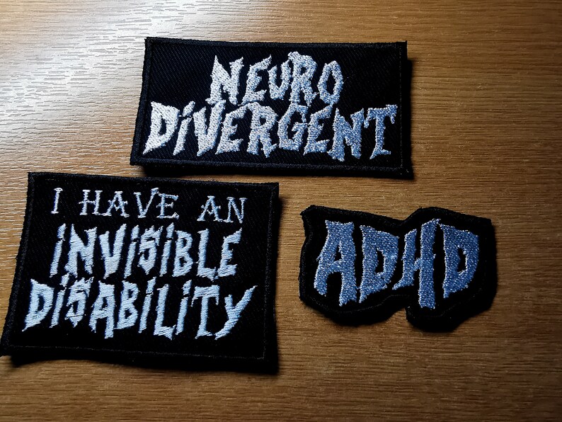 Pode incluir: Tr&ecirc;s patches de tecido preto com texto bordado branco. O patch superior diz "Neuro Divergente". O patch do meio diz "Eu tenho uma defici&ecirc;ncia invis&iacute;vel". O patch inferior diz "TDAH".