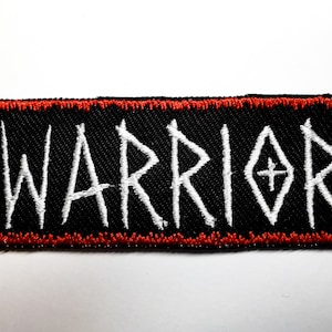 Könnte beinhalten: Schwarzer gestickter Aufnäher mit rotem Rand. Der Aufnäher trägt die Aufschrift "WARRIOR" in weißen Buchstaben.