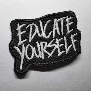 May include: Black patch with white embroidered text that reads "EDUCATE YOURSELF". The patch has a unique shape with a black border. The text is in a bold, handwritten style.