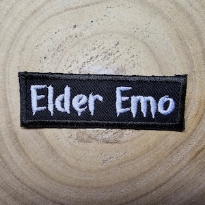 May include: Black embroidered patch with white text that reads "Elder Emo".