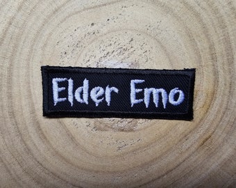 May include: Black embroidered patch with white text that reads "Elder Emo".