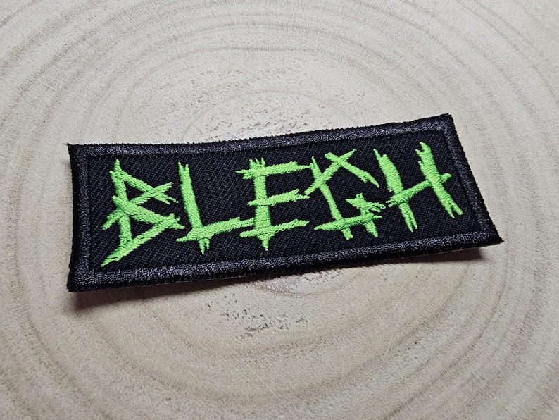 May include: Black and green embroidered patch with the word "BLEGH" in a stylized font.