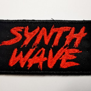 Puede incluir: Parche rectangular negro con las palabras "SYNTH WAVE" bordadas en rojo, con un estilo de pincelada. El parche tiene un borde negro y está diseñado para ropa o accesorios.