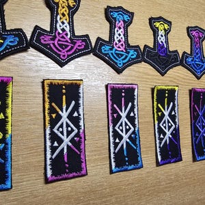 May include: Embroidered patches displaying the Mjolnir hammer and geometric symbols. The patches feature a range of colours, including blue, purple, yellow, and pink, with detailed knotwork designs on a black background.