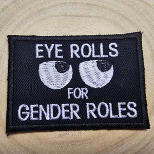 May include: Black embroidered patch with white text that reads "Eye Rolls for Gender Roles". Two white embroidered eyes are above the text.