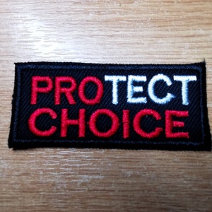 Könnte beinhalten: Schwarzer gestickter Aufnäher mit den Worten "PROTECT CHOICE" in weißer und roter Schrift.