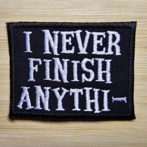 Può includere: Toppa ricamata nera con testo bianco che recita "Non finisco mai niente".