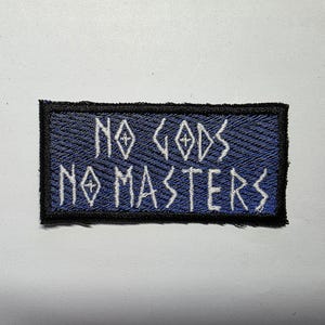 May include: A rectangular patch with the embroidered text "NO GODS NO MASTERS" in white, stylized lettering. The patch has a blue background with a textured pattern and a black border.