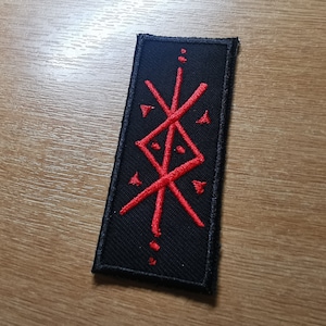 May include: A black embroidered patch with a red symbol. The symbol is a stylized design of intersecting lines and dots.