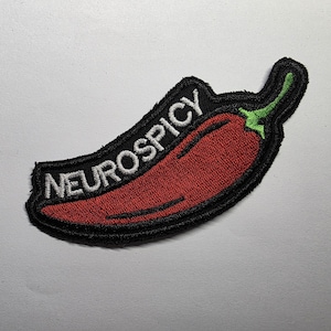 Op de afbeelding: Een geborduurde patch in de vorm van een rode chilipeper met een groene steel. De patch heeft een zwarte rand en de witte tekst NEUROSPICY is langs de bovenste curve van de peper geborduurd, wat zorgt voor een opvallend grafisch ontwerp.