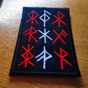 May include: A black fabric patch with red and white embroidered runes. The runes are arranged in three rows of three.