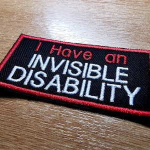 May include: A black patch with red stitching around the edges. The text "I Have an Invisible Disability" is embroidered in white.