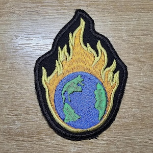 May include: A black patch with an embroidered image of a blue globe engulfed in yellow flames. The globe has green continents.