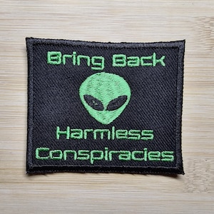 May include: Black embroidered patch with green text and a green alien graphic. The text reads "Bring Back Harmless Conspiracies".
