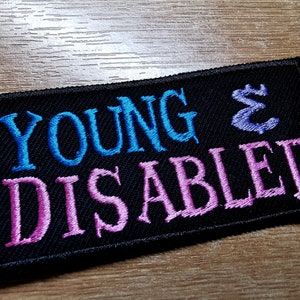 Può includere: Toppa ricamata nera con il testo "YOUNG & DISABLED" in lettere blu e rosa.