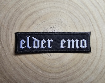 May include: Black embroidered patch with white text that reads "elder emo".