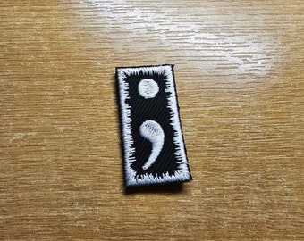 May include: White embroidered semicolon on a black fabric patch with white stitching around the edges.