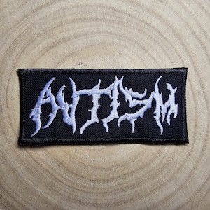 Peut inclure: Un patch brodé noir avec le mot "ANTHEM" en lettres blanches. Les lettres sont dans une police de caractères stylisée, métallique.