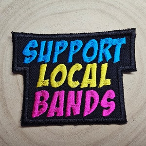 May include: Black embroidered patch with the text "Support Local Bands" in blue, yellow, and pink lettering.