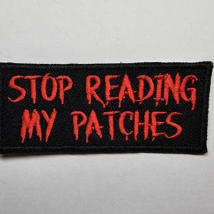 May include: Black fabric patch with red embroidered text that reads "STOP READING MY PATCHES".