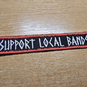 Puede incluir: Parche bordado rojo y negro con texto blanco que dice "SUPPORT LOCAL BANDS".
