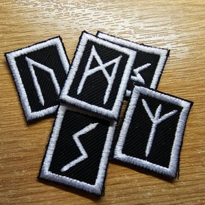 Op de afbeelding: Vijf zwarte stoffen patches met witte geborduurde runen. De runen zijn vierkant met een witte rand.