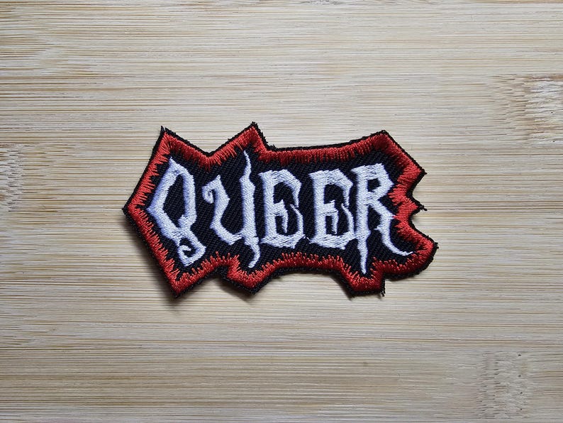 Peut inclure: Patch brod&eacute; rouge et noir avec le mot "QUEER" en lettres blanches.